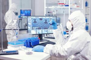 Medicine engineer with face mask and coveall looking at blood samplein lab. Doctor working with various bacteria and tissue, pharmaceutical research for antibiotics against covid19. photo