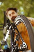 Detailed shot of bicycle wheel rubber chain being examined and maintained by young healthy caucasian man outdoor. Image showing close-up view of bike tire and pulley wheels in yard. photo