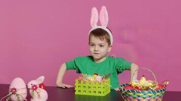 Sweet young boy making colorful arrangements for Easter holiday festivity, putting painted eggs in a handcrafted basket. Ecstatic joyful kid using crafting materials to create decorations. Camera A. photo