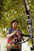 Sports-loving black woman holding professional equipment for bike maintenance in home yard. Determined african american individual focuses on repairing bicycle with specialized tools photo