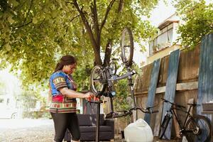 deportivo africano americano hembra utilizando miniordenador y profesional herramientas para servicio moderno bicicleta. joven activo negro mujer investigando para bicicleta mantenimiento instrucciones en ordenador portátil. foto