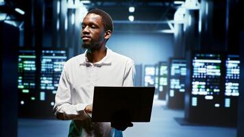 African american repairman using laptop to review energy consumption across server cabinets components. Manager making sure data center equipment temperature sensors are performing flawlessly photo