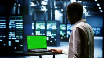 Supervisor using green screen laptop to inspect supercomputers doing intense computations. Professional preventing strain on data center hardware caused by AI applications driving up power usage photo