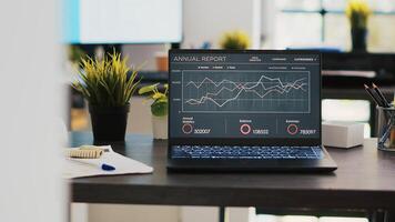 Business graphs and figures on laptop left open on desk in empty workspace. Economic annual report charts on notebook screen in company financial department office, panning shot photo