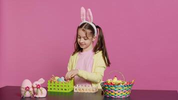 Smiling happy schoolgirl presenting a handmade decorated basket in studio, making easter holiday preparations against pink background. Young child showing handcrafted arrangements. Camera A. photo