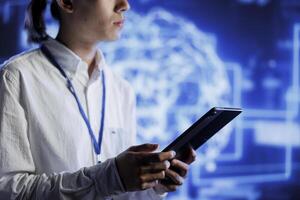 Admin using tablet in server farm to maintenance artificial intelligence neural networks simulating human thought processes in computerized model. High tech facility worker does checkup on AI systems photo