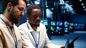 IT team running data center components diagnostic tests to determine and patch software issues. Workers using laptop and tablet to mend critical systems, checking for defects, close up photo