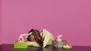 Exhausted little child decorating festive ornaments for easter sunday celebration, creating colorful cute arrangements with painted eggs. Tired girl yawning and falling asleep on the table. Camera A. photo