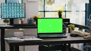 Focus on isolated screen laptop on company desk with computer desktop in blurry background showing stock exchange data. Chroma key notebook and trading platform displayed on PC screen in the back photo