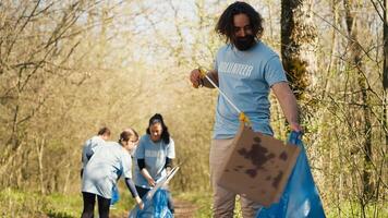 Man activist using tongs to grab garbage and plastic waste, picking up trash and cleaning the forest area. Volunteer sorting rubbish and recycling it, preserving the nature. Camera A. photo