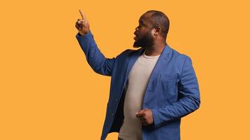 Salesman pointing upwards with finger doing recommendation, talking with audience. BIPOC person looking up, showing copy text, isolated over yellow studio background, camera B photo