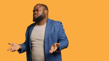 Uncaring man shrugs shoulders, showing indifference and apathy while talking with friend. Careless person doing nonchalant indifferent hand gesturing during conversation, studio background, camera A photo