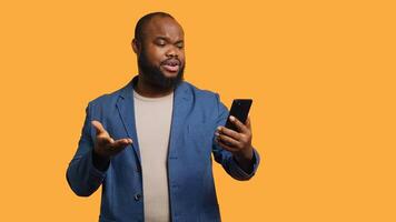 Upbeat man having friendly conversation with friends during teleconference meeting using smartphone, studio background. BIPOC person has fun catching up with mates during online videocall, camera A photo