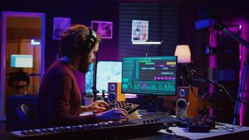 Music producer playing electronic piano notes and recording audio to adjust sound levels and create a soundtrack. Creative artist does mixing and mastering for his new songs in home studio. Camera B. photo