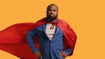 African american superhero flying with red cape, isolated over studio background, flexing muscles. Man wearing cloak posing as hero in costume showing courage and strength, camera B photo