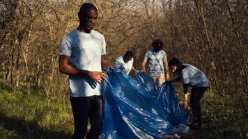 diverso voluntarios coleccionar basura y basura desde el bosque área, luchando ambiental contaminación y conservación. grupo de activistas limpieza arriba el bosque, reciclaje el plastico desperdiciar. cámara b. foto