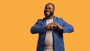 Portrait of jolly friendly african american man doing heart symbol shape gesture with hands. Cheerful nurturing BIPOC person showing love gesturing, isolated over studio background, camera B photo