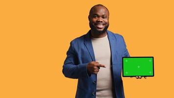 Upbeat african american man holding green screen tablet, doing recommendation. Cheerful BIPOC person pointing towards mockup device, giving positive feedback, studio background, camera B photo