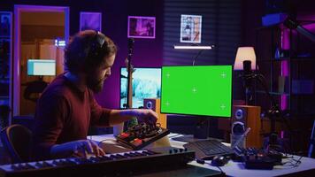 Audio engineer learning to mix piano notes with mixing console, watches online lesson tutorials on greenscreen monitor display. Music producer creating soundtracks, learns editing skills. Camera B. photo