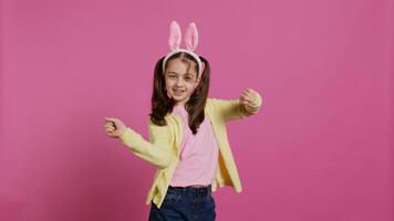 confidente alegre niña demostración danza se mueve en el estudio, sensación alegre y positivo acerca de Pascua de Resurrección fiesta festividad. talentoso niño bailando alrededor y vistiendo conejito orejas. cámara b. foto