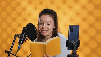 Media star filming vlog at work, reading book to record audiobook, studio background. Voice actor doing content creation while producing digital recording on novel using microphone, camera A photo