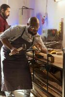 Craftsperson carving designs into wood using chisel and hammer next to coworker. Artisan shaping wooden pieces using protective equipment to prevent workplace accidents, helped by apprentice photo