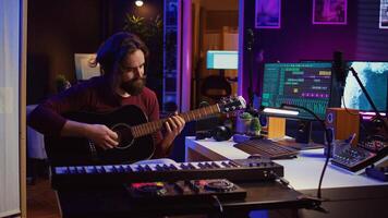 Music producer tuning his acoustic guitar before playing instrument, recording and mixing tunes to create new soundtracks. Singer composing a song using electronic panel controls. Camera B. photo