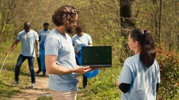 Team of eco friendly activists using pc with isolated display in the woods, volunteering to collect rubbish and plant trees for future generations. Environmental conservation. Camera A. photo