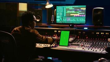 African american audio technician mixing and editing tracks with greenscreen on tablet, working in professional post production studio. Producer creating new tunes for his album. Camera B. photo