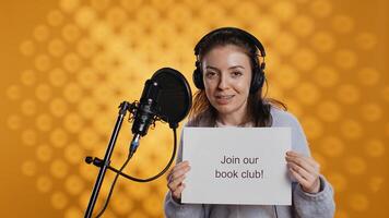 Joyous woman filming promotional for world book day using microphone, studio background. Happy content creator promoting reading, gaining awareness for literature importance, camera B photo