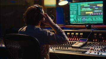 Sound designer working on track recording with audio professional software, operating technical equipment on panel board in control room. Audio engineer enhances music high quality. Camera A. photo