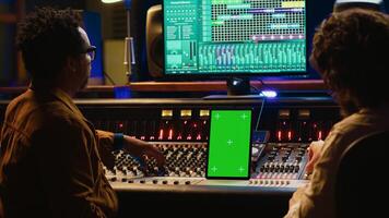 Team of producer and artist use tablet with mockup display in professional studio, mixing and mastering tracks after recording session. Experts working in control room with console. Camera A. photo