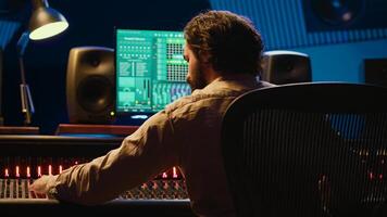 Sound designer mixing and mastering tracks on audio console in control room, using daw software on computer and editing files. Technician creating new music in professional studio. Camera A. photo