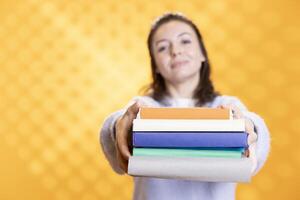 retrato de sonriente mujer ofrecimiento pila de libros, recomendando leyendo pasatiempo para relajación propósitos. radiante adicto a los libros persona con apilar de novelas en brazos haciendo aprobación, estudio antecedentes foto