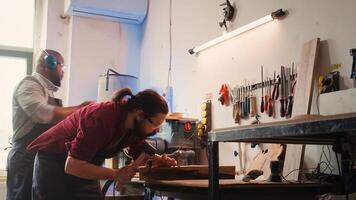 Woodworker using bench vise to hold lumber block, carving intricate designs into wood using chisel and hammer. Craftsperson using vice tool to clamp piece of wood, shaping log with tools, camera B photo