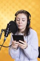 Woman doing voiceover word for word reading of ebook on ereader to produce audiobook. Narrator using storytelling skills while reading text from tablet, recording novel, studio background photo