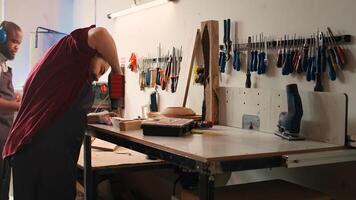 Woodworker in assembly shop using power drill to create holes for dowels in wooden board. Carpenter sinking screws into wooden surfaces with electric tool, doing precise drilling for seamless joinery, camera B photo