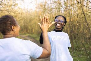 africano americano mujer compartiendo alto cinco y siendo contento con el resultados de el equipo, felicitando cada otro después refinamiento bosque camada limpiar. orgulloso y satisfecho con su trabajar. foto