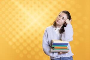 Portrait of relaxed woman daydreaming while holding pile of books, enjoying reading hobby. Person with stack of novels in arms caught in reverie while enjoying leisure time, studio background photo