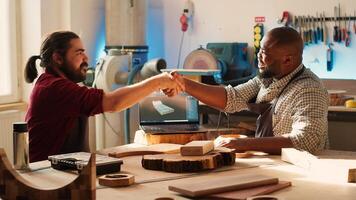 Cabinetmaker shaking colleague hand after finishing using CAD software on laptop to design wooden objects. Carpenters congratulating each other for job well done in furniture assembling shop, camera A photo