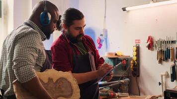 Craftsperson and colleague look over technical schematics to make commissioned wooden object. Manufacturer and coworker analyze blueprints to execute furniture assembling woodworking project, camera A photo