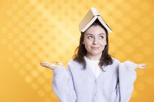 Woman with opened book on head acting zany, portraying having fun concept, isolated over studio background. Bookworm wearing novel and as hat, enjoying life, clowning around, feeling excited photo