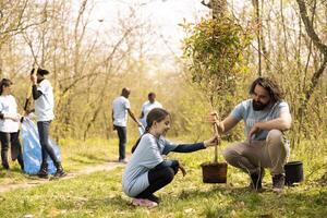 hombre y pequeño niña equipo arriba y planta un árbol juntos en el bosque, conservación el natural ambiente. personas trabajar como voluntario a ayuda bosque ecosistema crecer y preservar fauna silvestre. foto