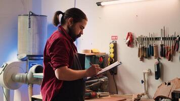 Carpenter drawing blueprints on notepad in studio, transforming creative ideas into tangible wood art pieces. Artisan looking at technical schematics to execute woodworking projects, camera A photo