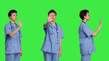 Health specialist with blue scrubs showing stop sign in studio, standing against greenscreen backdrop. Nurse expressing denial and refusal with warning forbidden symbol, denying something. Camera B. photo