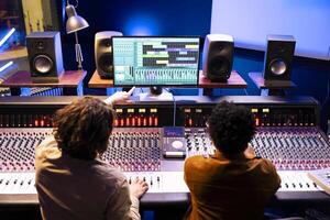 audio ingeniero y artista colaborando en nuevo canciones para popular álbum, composición y edición melodías con mezcla consola y digital software. músico trabajando con técnico en registros en estudio. foto