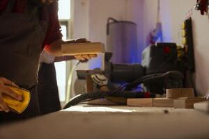 Man in assembly shop using sandpaper for sanding wooden surface before painting it, ensuring adequate finish. Carpenter using abrasive sponge to fix surface damages suffered by wood photo