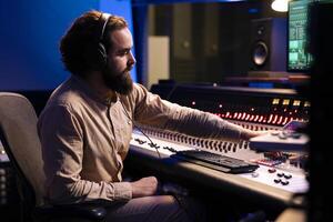 Mixer producer listening to his audio recordings and editing tracks in post production, working with technical gear and mixing console. Expert integrating amplifying sounds using motorized faders. photo