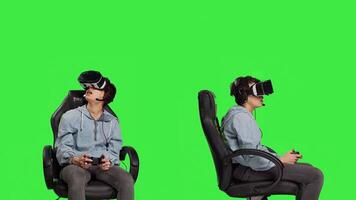 mujer jugando juegos en consola con controlador y vr auriculares, sentado en contra pantalla verde fondo. jugador teniendo divertido con en línea torneo, virtual realidad interactivo ciberespacio. cámara b. foto