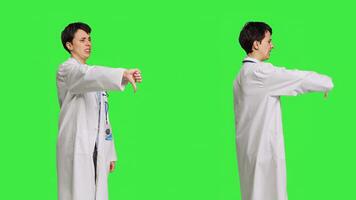 Displeased physician showing thumbs down symbol against greenscreen backdrop, expresses negativity and rejection. Doctor feeling dissatisfied and disagreeing with an idea, dislike sign. Camera B. photo